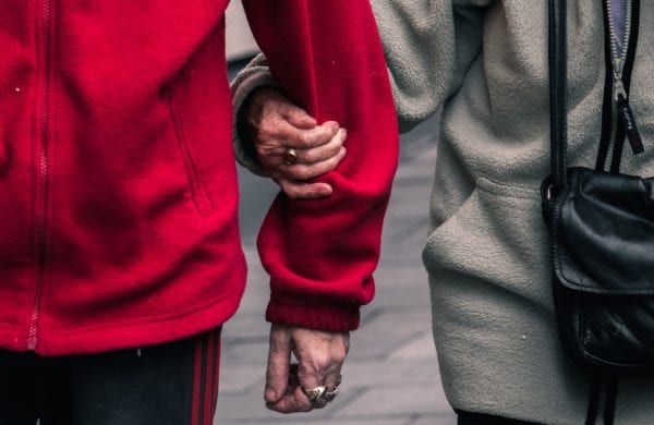 two elderly people supporting each other by the arm