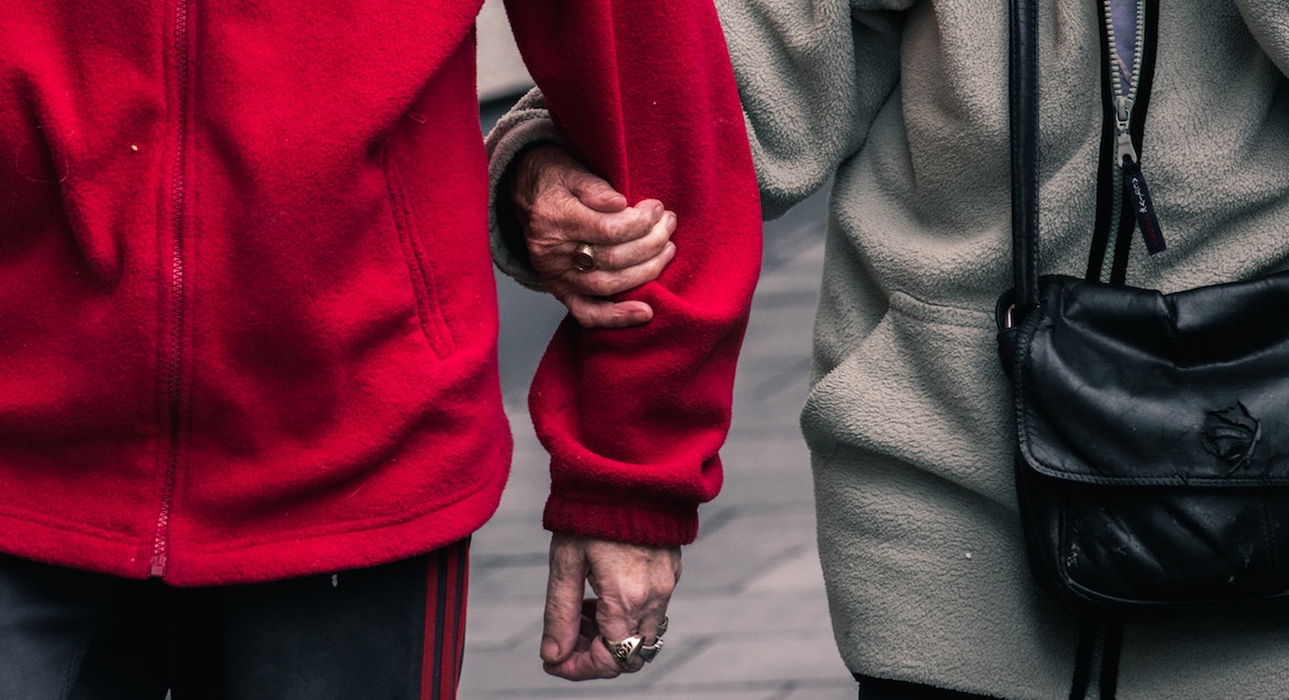 two elderly people supporting each other by the arm