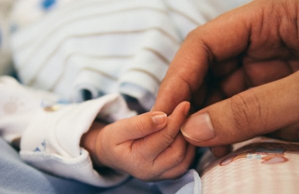 an adult holds a baby's hand
