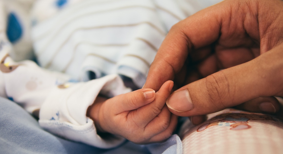 an adult holds a baby's hand