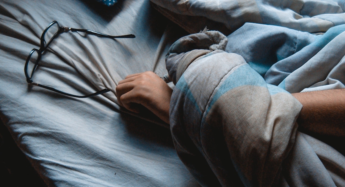 an arm lying on a bed with glasses