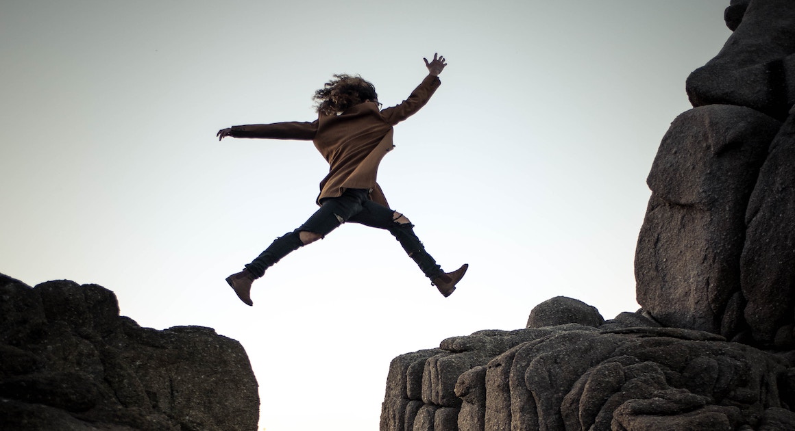 a woman jumping across a crevasse