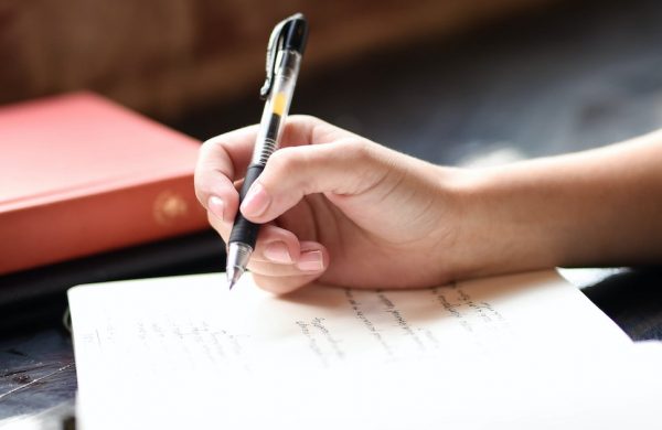 hand holding a pen above a pad with writing on it