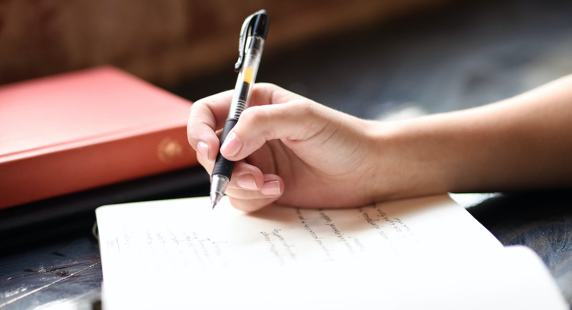 hand holding a pen above a pad with writing on it